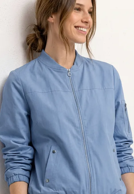 Frau trägt hellblaue, taillierte Bomberjacke mit Reißverschluss, Stehkragen und angenähten Taschen.