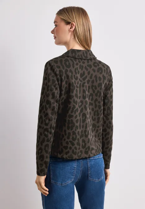 Eine Frau von hinten trägt eine khakifarbene Jacke mit Leopardenmuster und blaue Jeans.