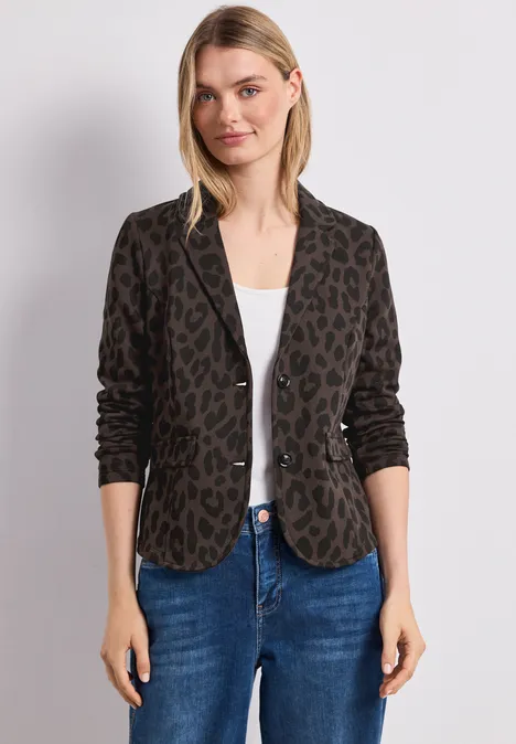 Frau in Leo-Blazer, weißem Top und Jeans vor hellem Hintergrund.