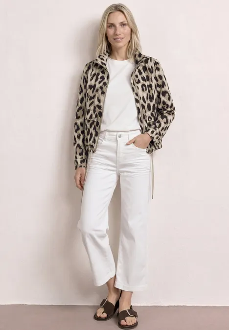 Vrouw draagt luipaardjas, wit t-shirt, witte wijde jeans en sandalen.