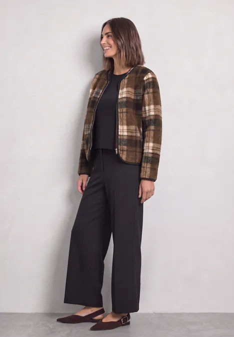 Femme en veste marron à carreaux, pull noir, pantalon large noir et ballerines marron.