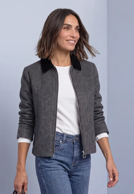 Femme souriante en veste grise à col noir, t-shirt blanc et jean bleu, marchant.