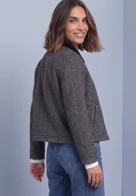 Femme en veste grise et jean, vue de dos, tournant la tête vers l'appareil avec un sourire