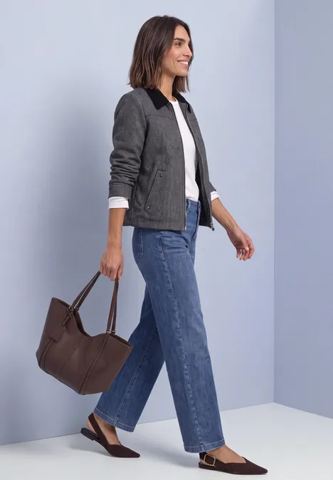 Femme en jean, t-shirt blanc et veste grise, portant un sac marron, marchant de profil.