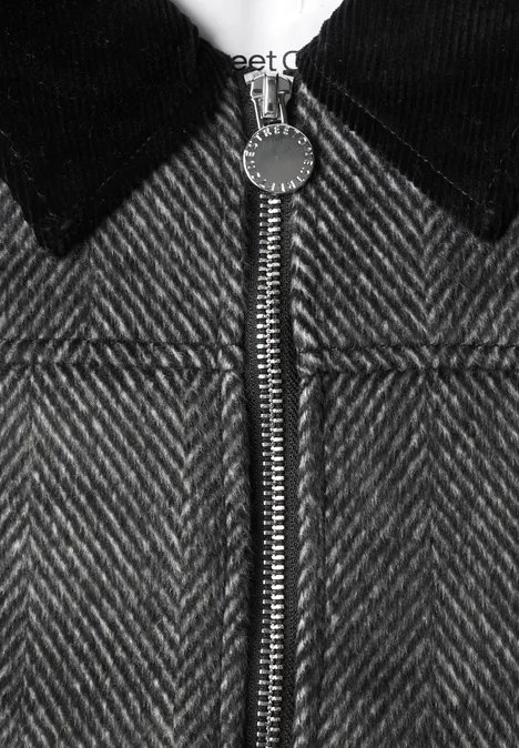 Gros plan d'une veste chevrons grise avec col noir et fermeture éclair argentée.