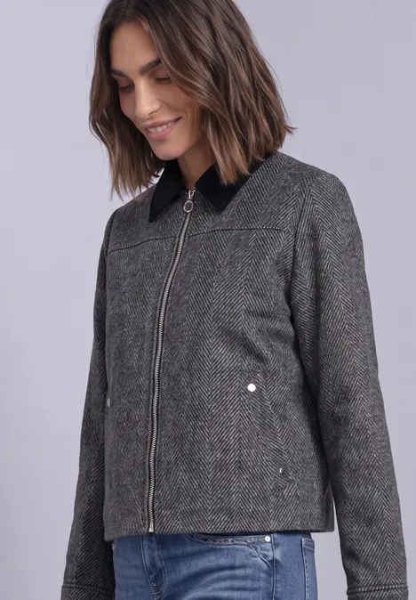 Femme portant une veste grise cintrée zippée avec un col montant noir.