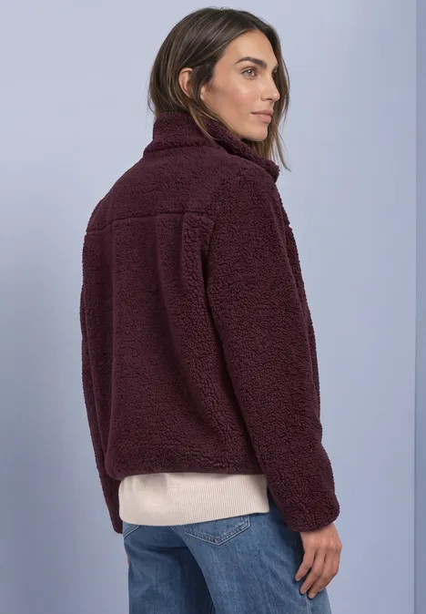 Teddy-Jacke mit Stehkragen und Zipper rustic rouge Frau von hinten in dunkellila Fleecejacke, hellem Pullover und Jeans vor hellem Hintergrund.