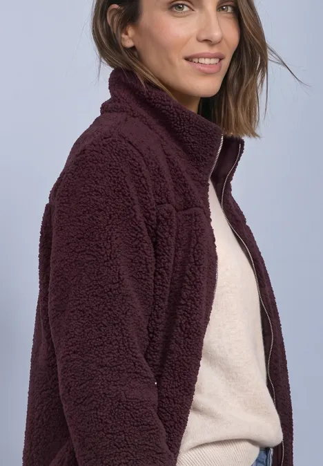 Teddy-Jacke mit Stehkragen und Zipper rustic rouge Frau in bordeauxrotem Teddy-Fleece-Pullover mit Reißverschluss, seitlich lächelnd.
