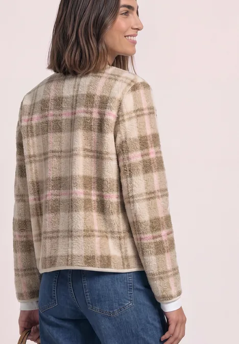 Femme vue de dos portant un blazer beige à carreaux roses et un jean bleu.
