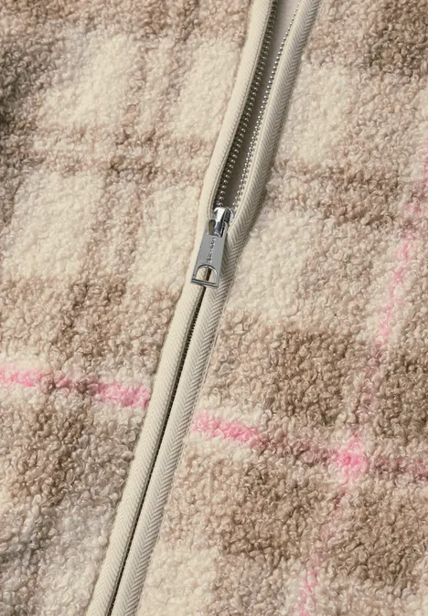 Gros plan d’une fermeture éclair gris-beige sur tissu en laine marron à carreaux, fines rayures roses.