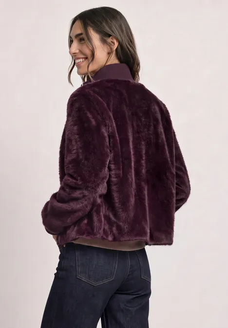 Blouson van imitatiebont met gebreide details en print rustic rouge Frau trägt lila Plüschjacke und Jeans, schaut lächelnd über die Schulter.