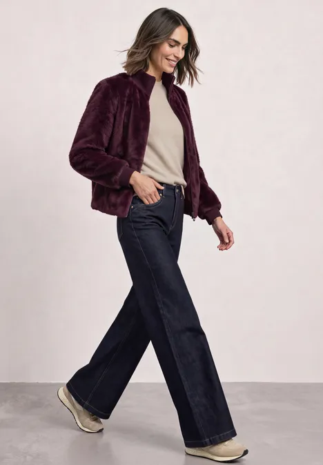 Blouson van imitatiebont met gebreide details en print rustic rouge Frau in bordeauxrotem Teddy-Mantel, weitem Jeans und Sneakern geht fröhlich zur Seite.