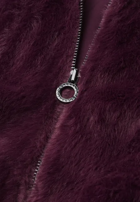 Blouson van imitatiebont met gebreide details en print rustic rouge Nahaufnahme eines silbernen Reißverschlussanhängers auf flauschigem, dunkelviolettem Stoff.