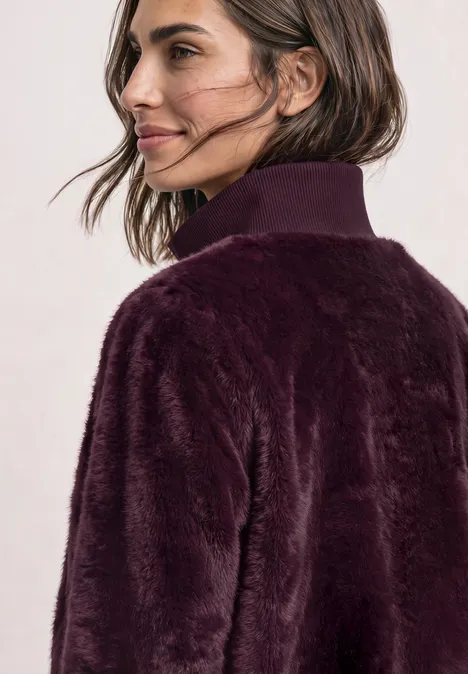 Blouson van imitatiebont met gebreide details en print rustic rouge Frau mit dunkelvioletter Kunstpelzjacke schaut lächelnd seitlich.