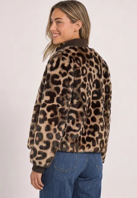 Frau im Leopardenmantel und Jeans, lächelt seitlich zur Kamera.