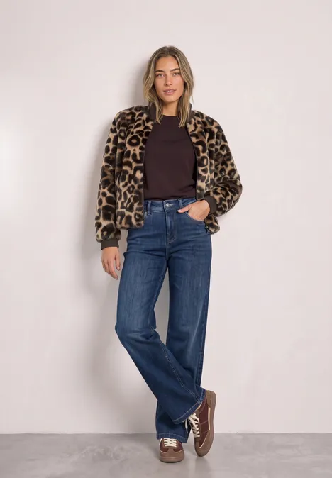 Frau in kurzer Jacke mit Leopardenmuster, dunklem Shirt, weiten Jeans und braunen Schuhen.