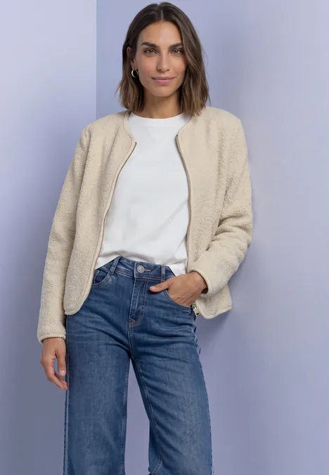 Veste en peluche à col rond et détails en velours côtelé Soft Fawn Beige Eine Frau in weißem Shirt, beiger Teddyjacke und Jeans vor lila Hintergrund.