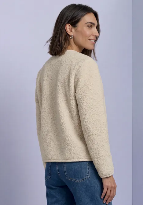 Veste en peluche à col rond et détails en velours côtelé Soft Fawn Beige Frau in beigefarbener Fleecejacke und Jeans, von hinten seitlich im Studio vor hellem Hintergrund