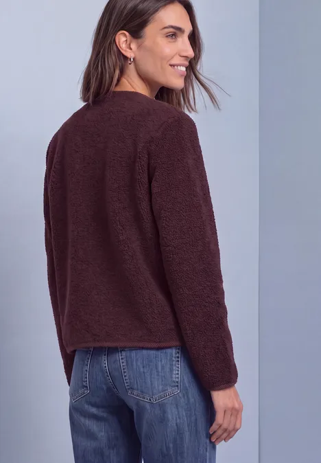 Une femme en jean et pull marron, vue de dos, tête tournée de profil.