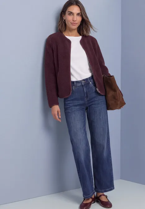 Femme en t-shirt blanc, veste bordeaux, jean large et ballerines avec un sac marron.