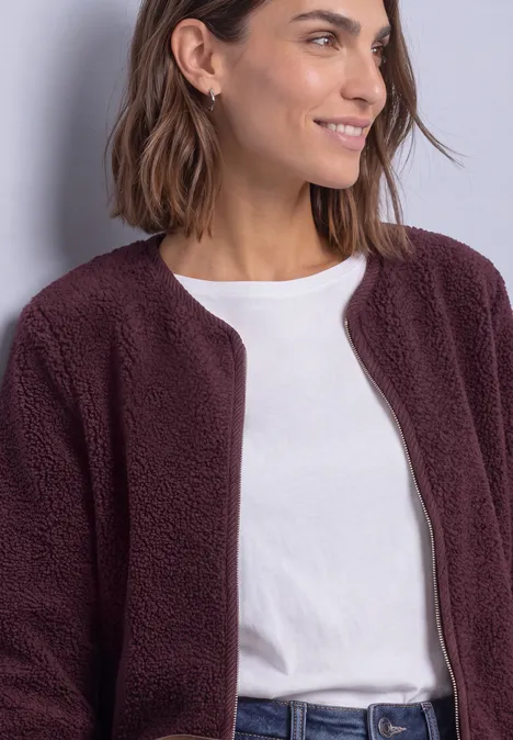Femme en t-shirt blanc et veste en fausse fourrure bordeaux, souriante, regard de côté