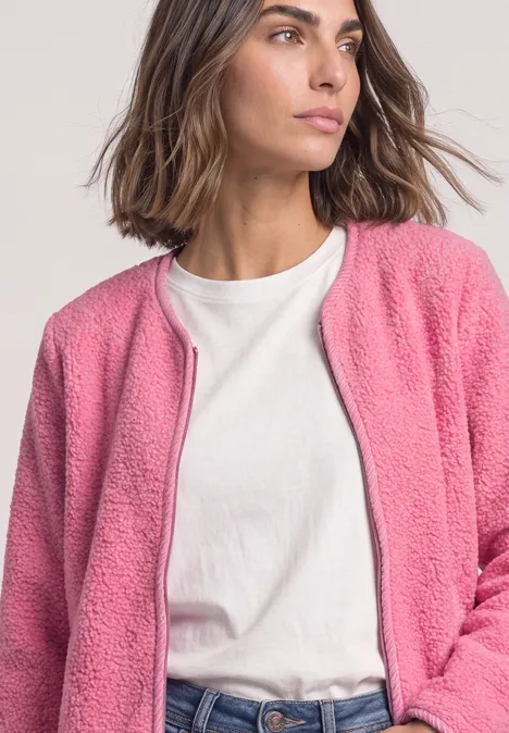 Une femme porte un T-shirt blanc et une veste polaire rose, le regard tourné sur le côté.