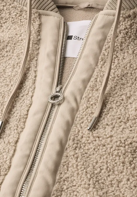 Detailaufnahme einer beigen Teddy-Fleecejacke mit Reißverschluss und Kordelzug.