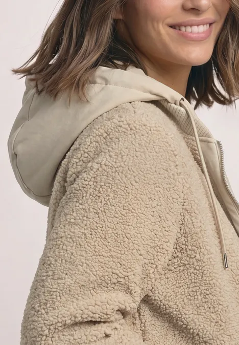 Nahaufnahme einer Frau in einer beigen Teddy-Fleecejacke mit Kapuze.