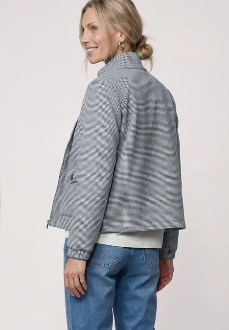 Rückansicht einer Person in grauer Jacke, blauer Jeans und lockerem Dutt.