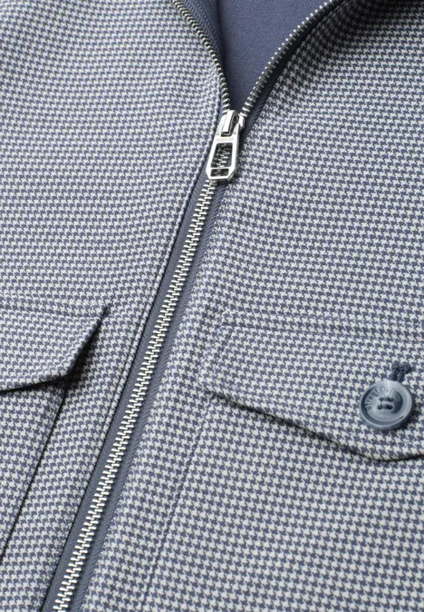 Nahaufnahme einer hellgrau-blauen, fein karierten Jacke mit Reißverschluss und Knopf-Tasche