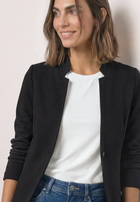 Blazer mit Reverskragen und Struktur Black Frau in schwarzer Jacke und weißem Shirt, lächelnd vor hellem Hintergrund.