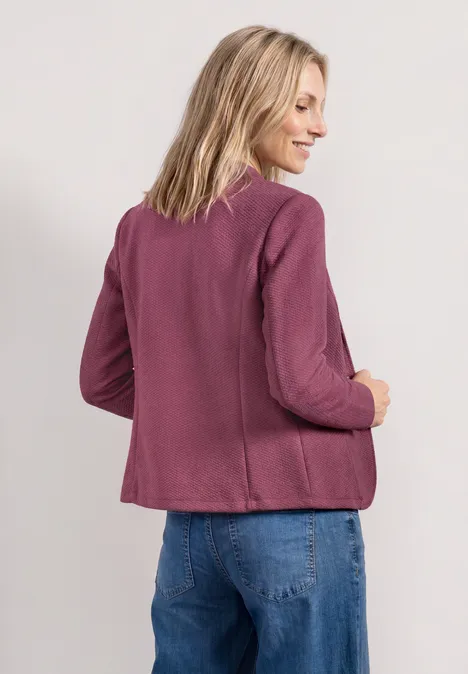Une personne de dos porte une veste violette et un jean bleu.