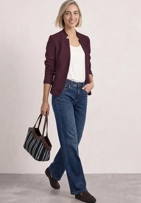Blazer mit Reverskragen und Struktur rustic rouge Eine Frau in weißem Top, bordeauxrotem Blazer und blauen Jeans hält eine gestreifte Tasche und lächelt.