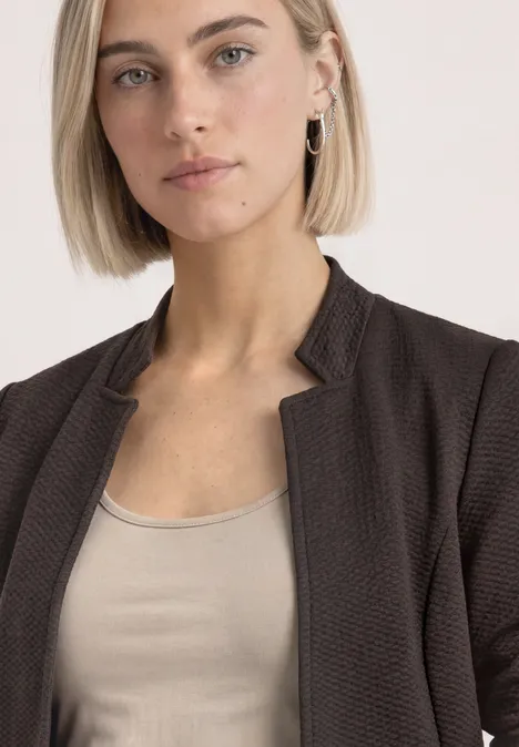 Blazer mit Reverskragen und Struktur black coffee mel. Frau mit kurzem blondem Haar trägt eine braune Jacke und ein beiges Top, Blick ruhig und direkt.