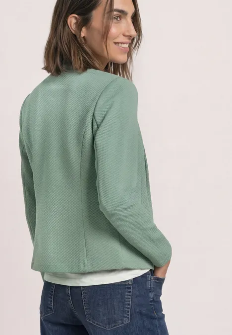 Blazer met reverskraag en structuur eucalyptus green Frau im grünen Blazer und Jeans, lächelt zur Seite und hat Hände in den Hosentaschen.