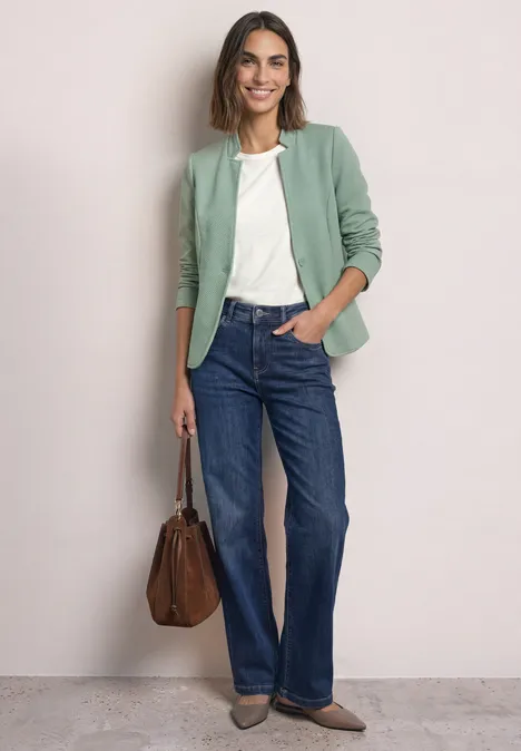 Blazer met reverskraag en structuur eucalyptus green Frau trägt grünen Blazer, weiße Bluse, blaue Jeans und hält eine braune Tasche.