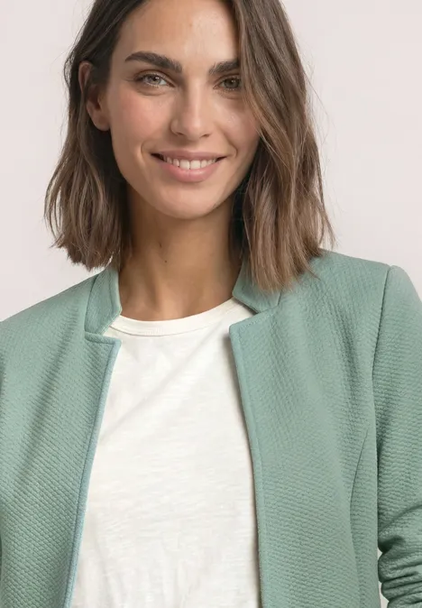 Blazer met reverskraag en structuur eucalyptus green Eine lächelnde Frau mit schulterlangen braunen Haaren trägt ein weißes T-Shirt und eine hellgrüne Strickjacke.