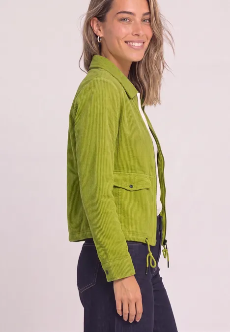 Veste en velours côtelé avec col chemise et fermeture à zip apple lime Frau trägt smaragdgrüne Jacke mit Klappentaschen und Kordelzug, lächelnd vor hellem Hintergrund.