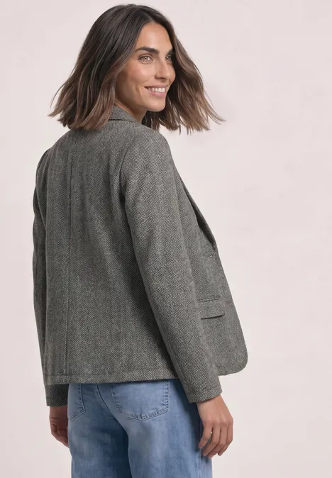 Eenvoudige blazer met reverskraag en patroon Black Frau in grauem Blazer und blauen Jeans schaut über die Schulter und lächelt.