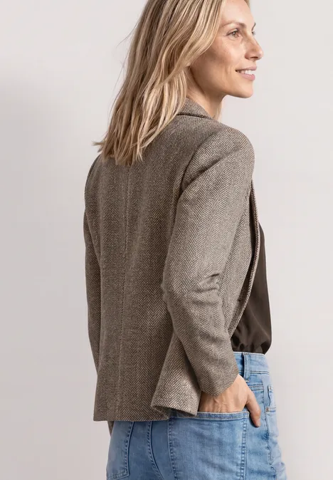 Eenvoudige blazer met reverskraag en patroon saddle brown Seitenansicht einer lächelnden Frau in grauem Blazer und Jeans, Hand in Tasche vor hellem Hintergrund.