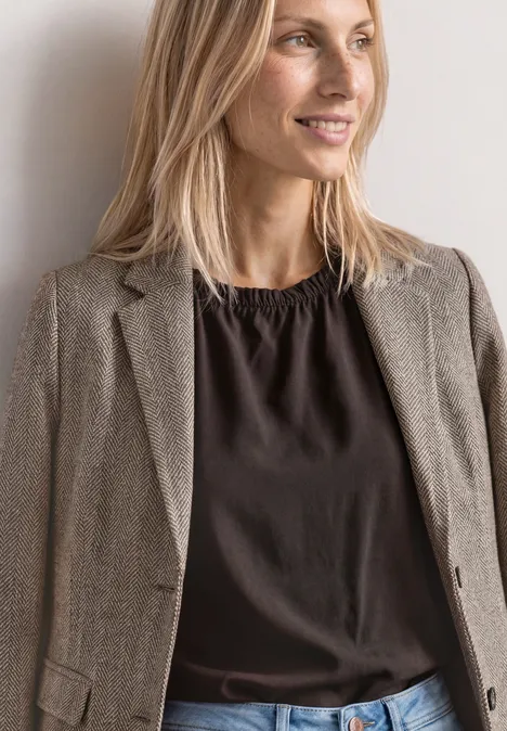 Eenvoudige blazer met reverskraag en patroon saddle brown Eine lächelnde blonde Frau in grauem Blazer und dunklem Top vor neutralem Hintergrund.