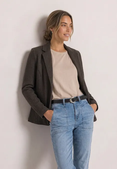 Eenvoudige blazer met reverskraag en patroon black coffee Eine junge Frau steht lächelnd in Casual-Outfit mit Blazer, T-Shirt und Jeans vor hellem Hintergrund.