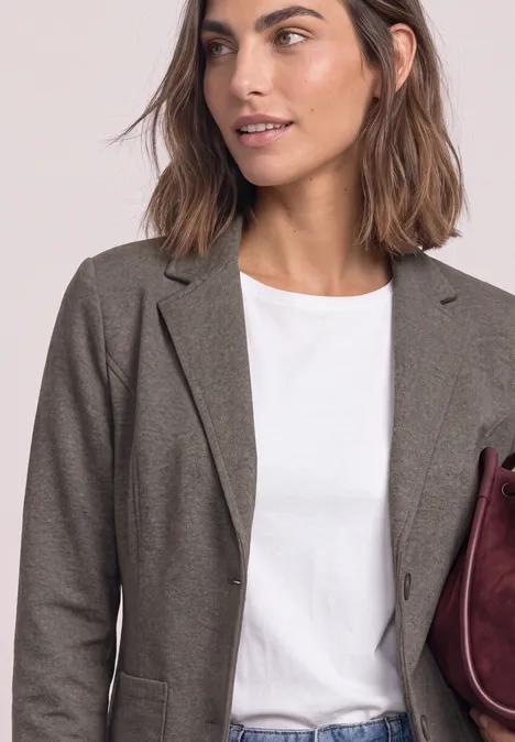 Frau in olivegrünem Blazer und weißem T-Shirt mit burgunderroter Tasche.
