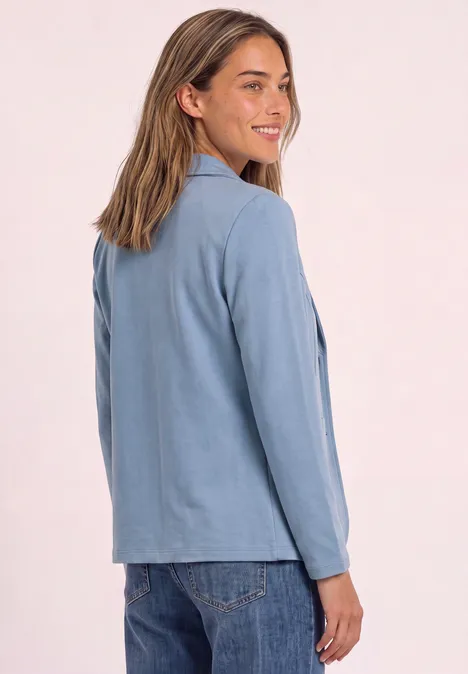 Blazer basique uni northern blue mel. Eine Frau in blauer Jacke und Jeans blickt lächelnd über die Schulter
