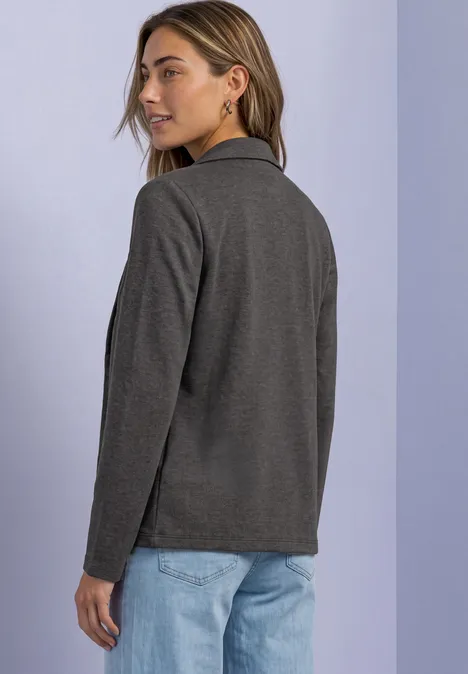 Blazer basique uni black coffee mel. Frau steht seitlich abgewandt, trägt grauen Blazer und hellblaue Jeans vor hellem Hintergrund.