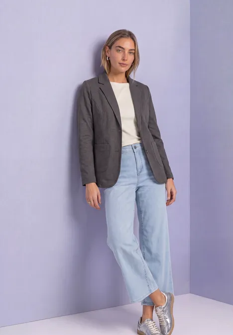 Blazer basique uni black coffee mel. Eine junge Frau steht vor lila Hintergrund in grauem Blazer, weißem T-Shirt, weiten Jeans und Sneakers.