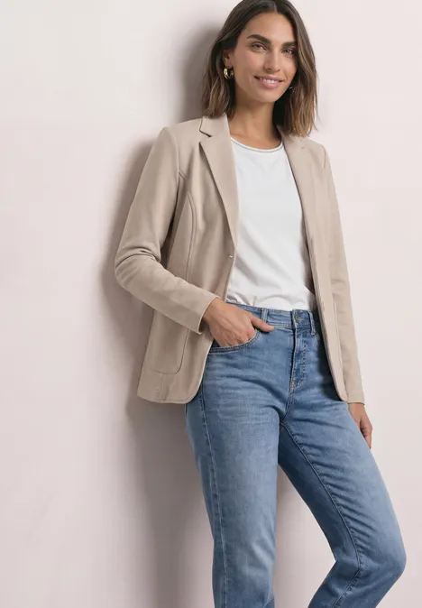 Basic Blazer in Unifarbe clay sand mel. Frau in beigem Blazer, weißem T-Shirt und blauen Jeans vor hellem Hintergrund.