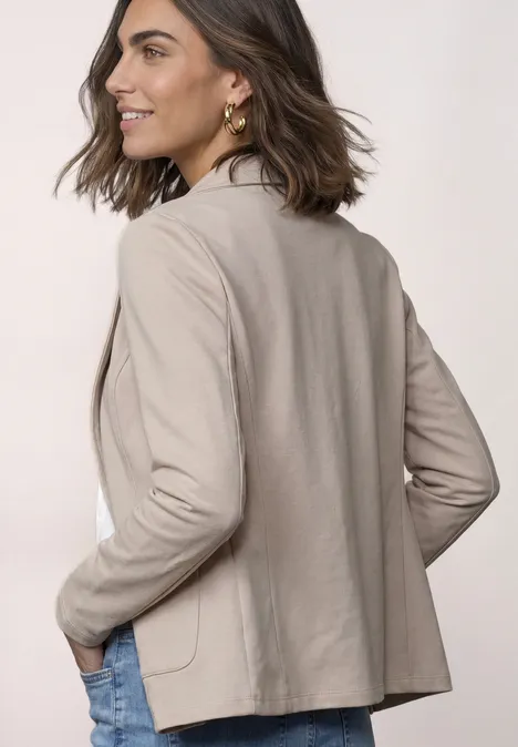 Basic Blazer in Unifarbe clay sand mel. Frau in beige Blazer schaut über die Schulter, Hände in den Taschen, leicht lächelnd.
