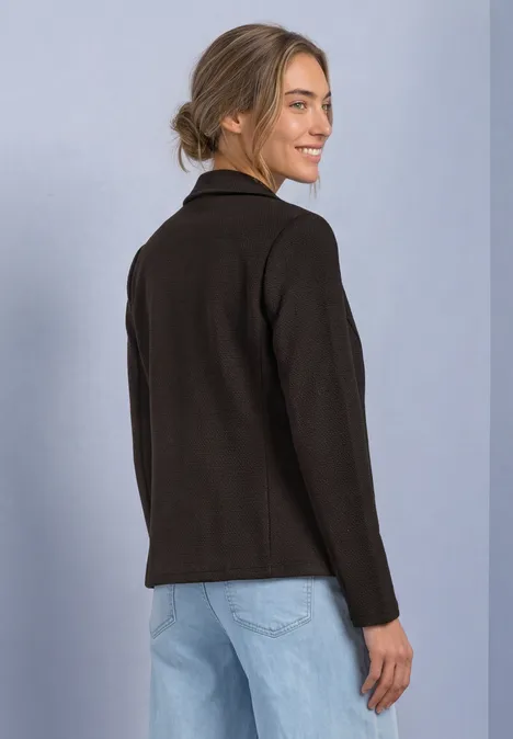 Frau in schwarzer Jacke und Jeans steht seitlich, schaut über die Schulter und lächelt.