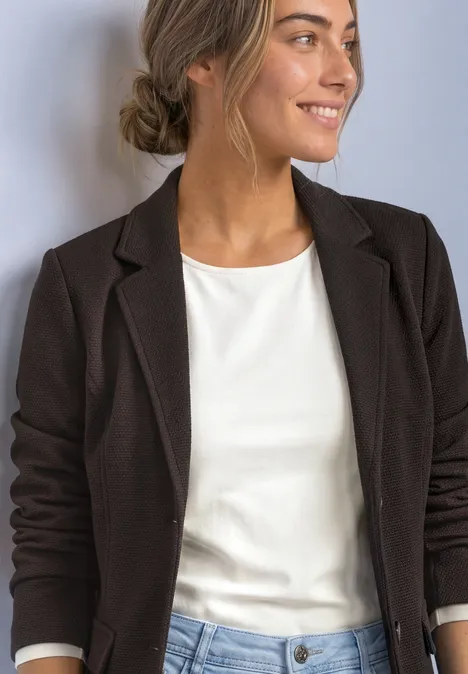 Eine Frau in schwarzem Blazer und weißem Oberteil lächelt seitlich.